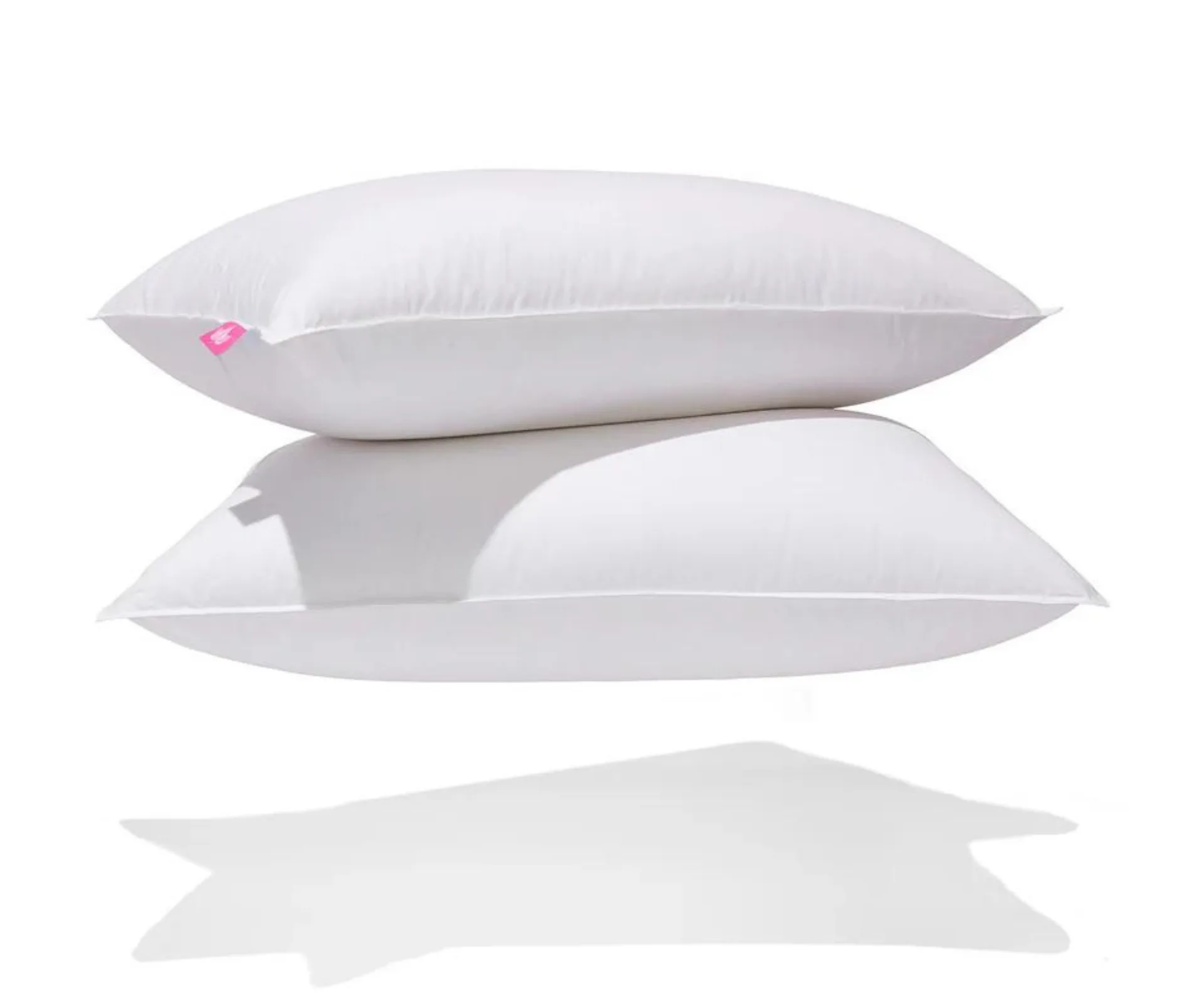 Two stacked white pillows with a small pink tag on the corner, casting a shadow against a white background.