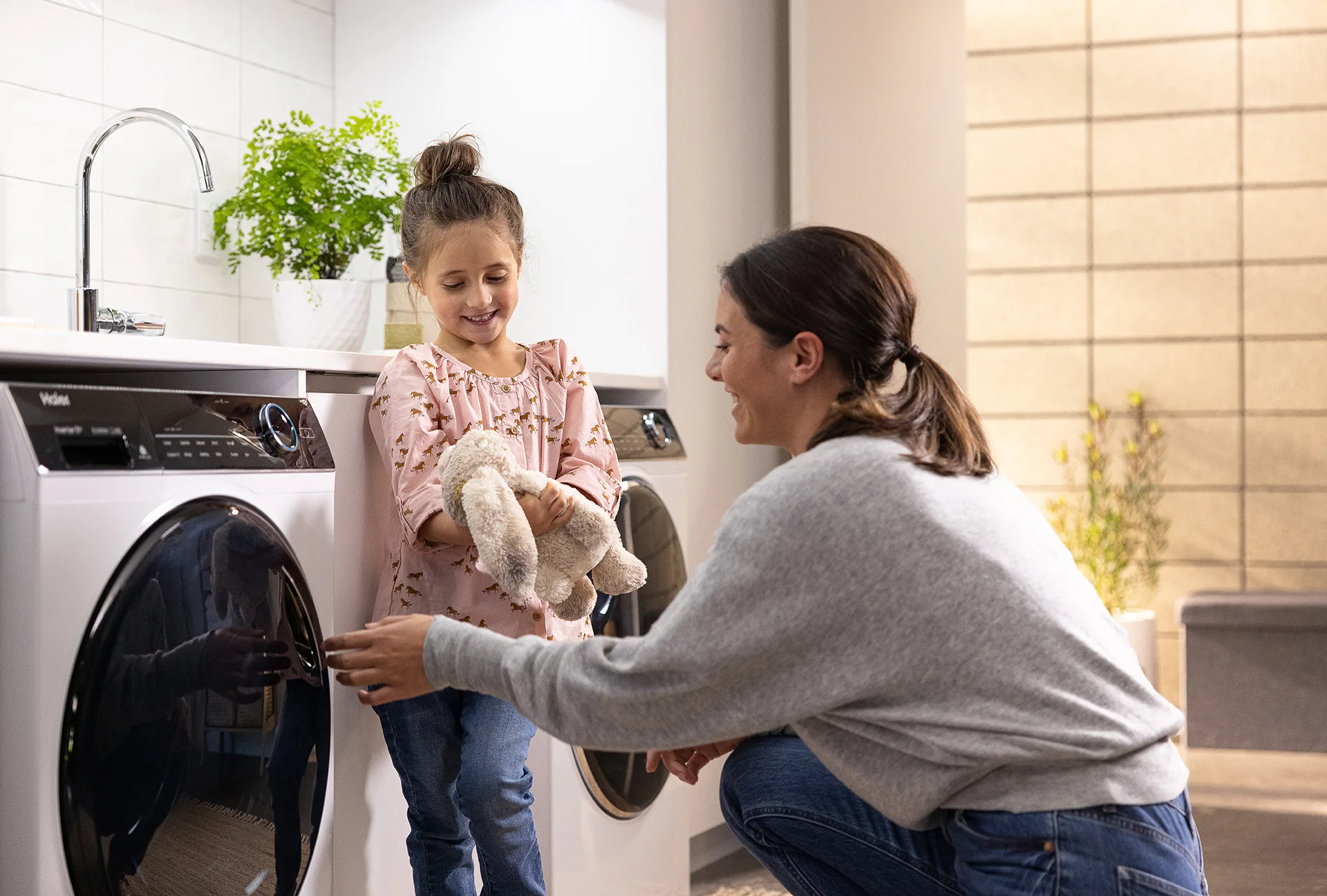 Mum and daughter with soft toy in laundry room