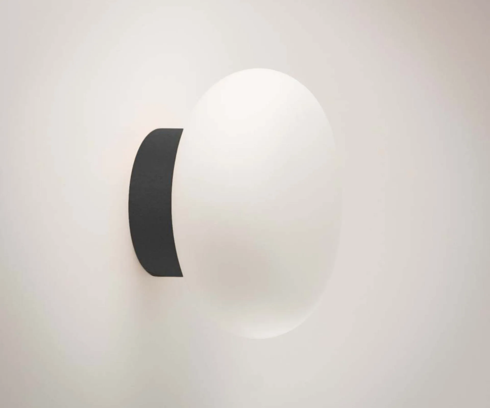 A round light pendant fixed to the wall on a sleek black base