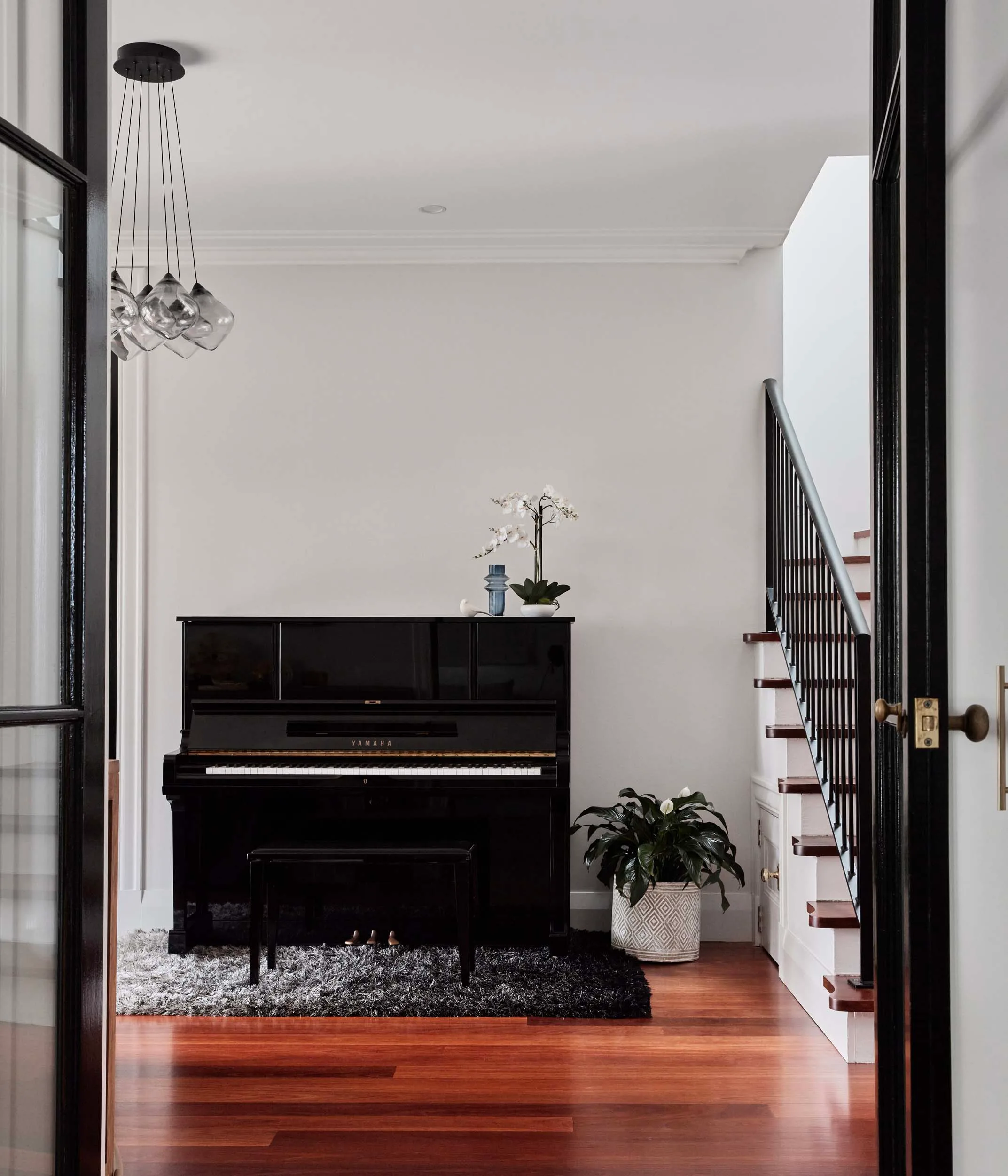 Through big black double doors in this harbourside home renovation lays a large black grand piano