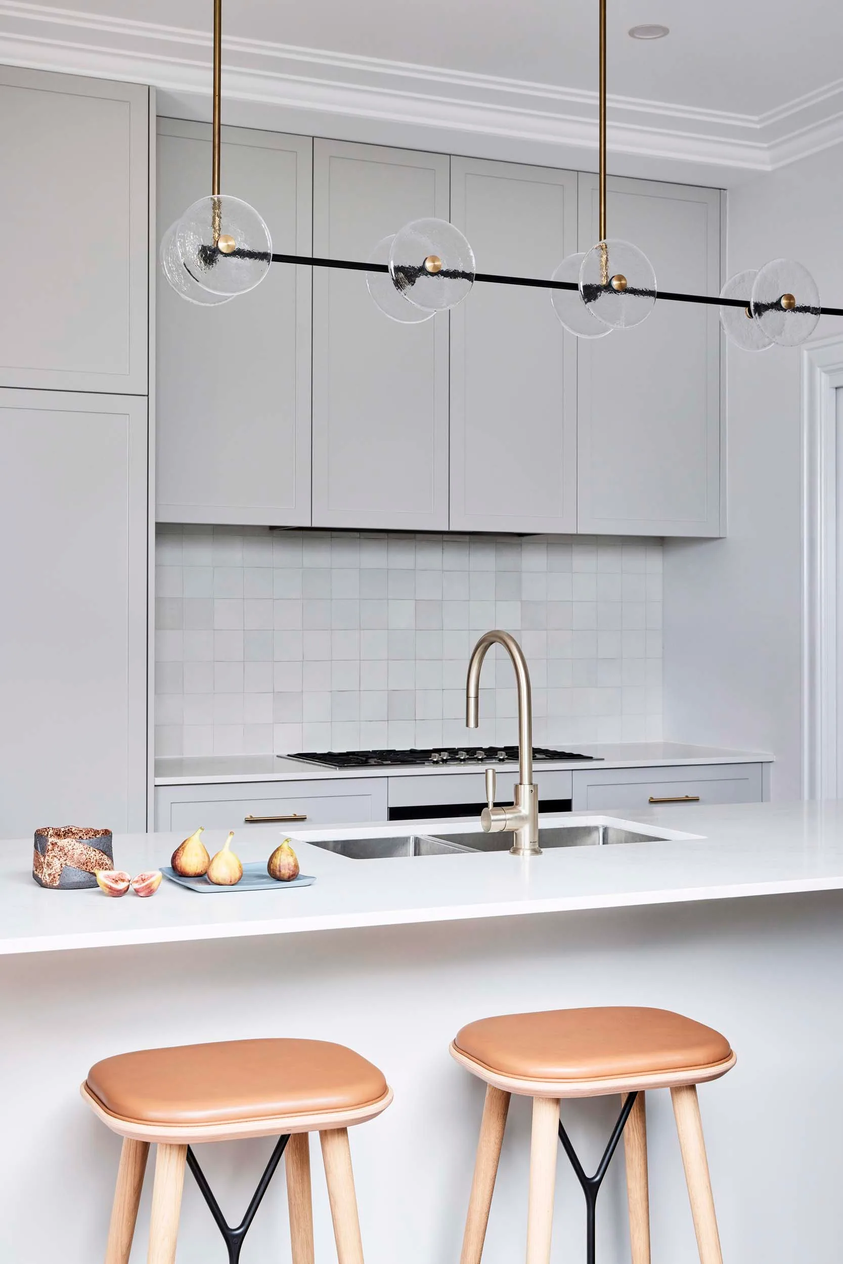 A white kitchen with round bulb pendant lights and brown leather bar stools