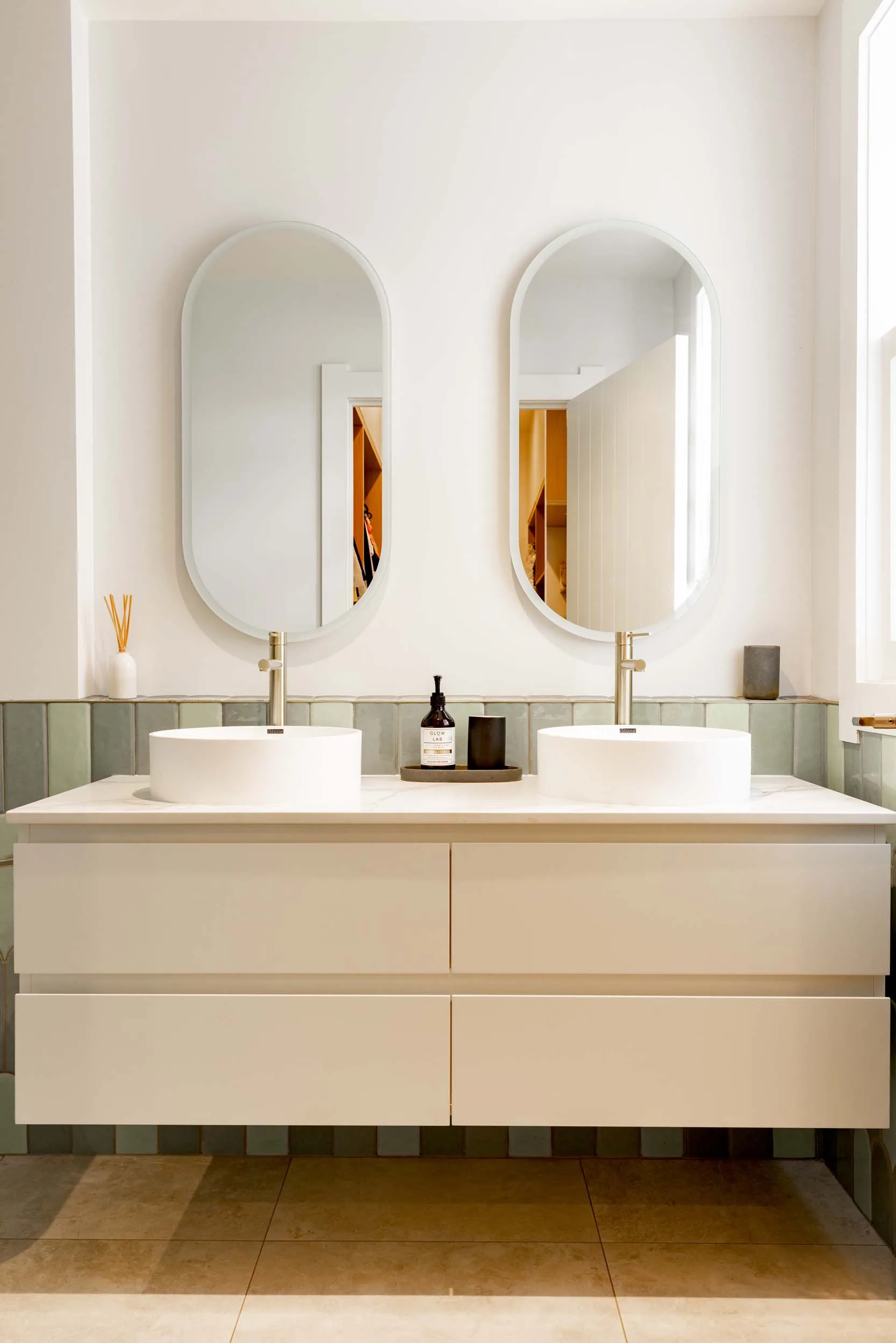 A white bathroom vanity with two oval mirrors