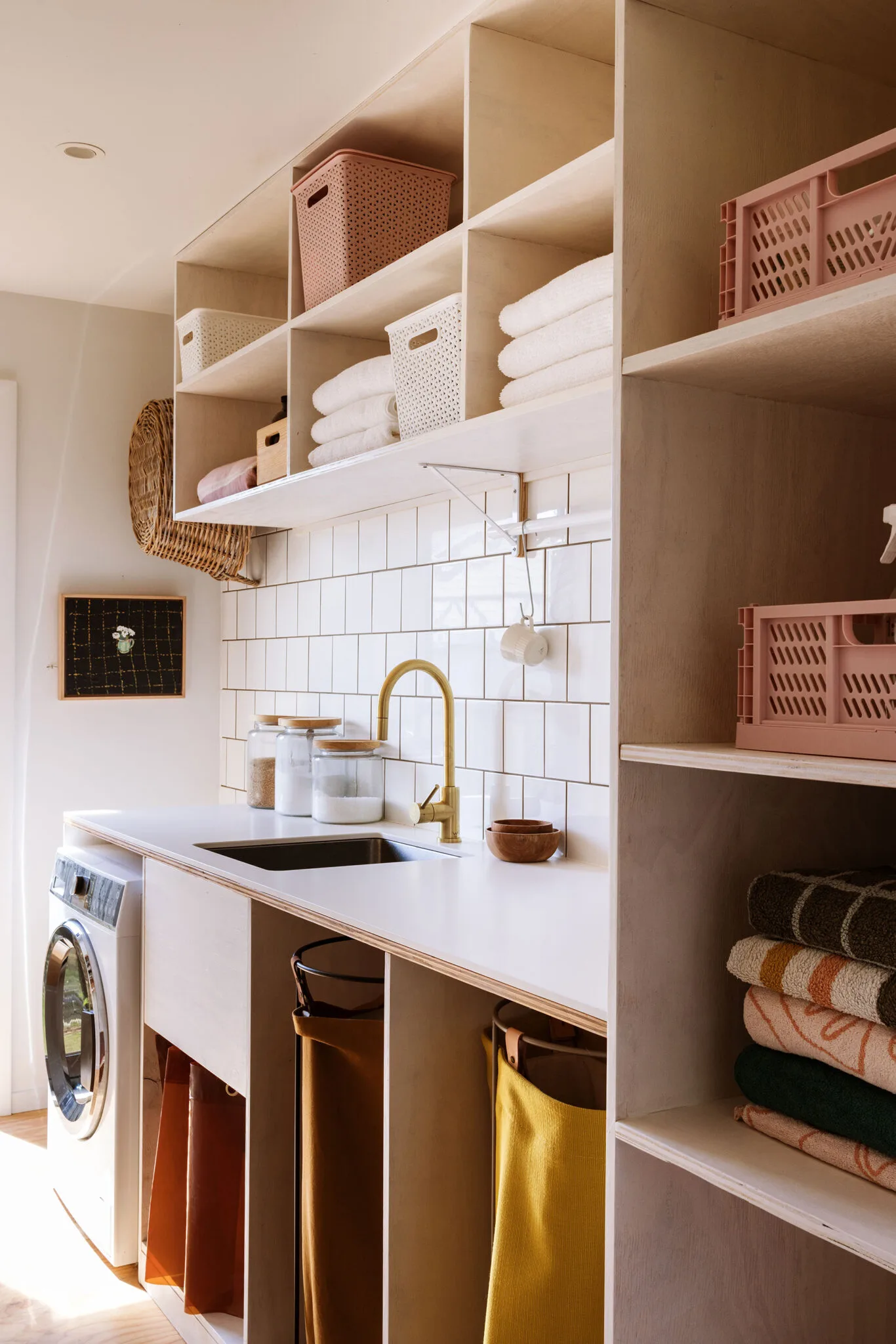 A recently renovated laundry with a white tiled splashback, and plenty of storage for clean towels, cleaning products, and laundry hampers.