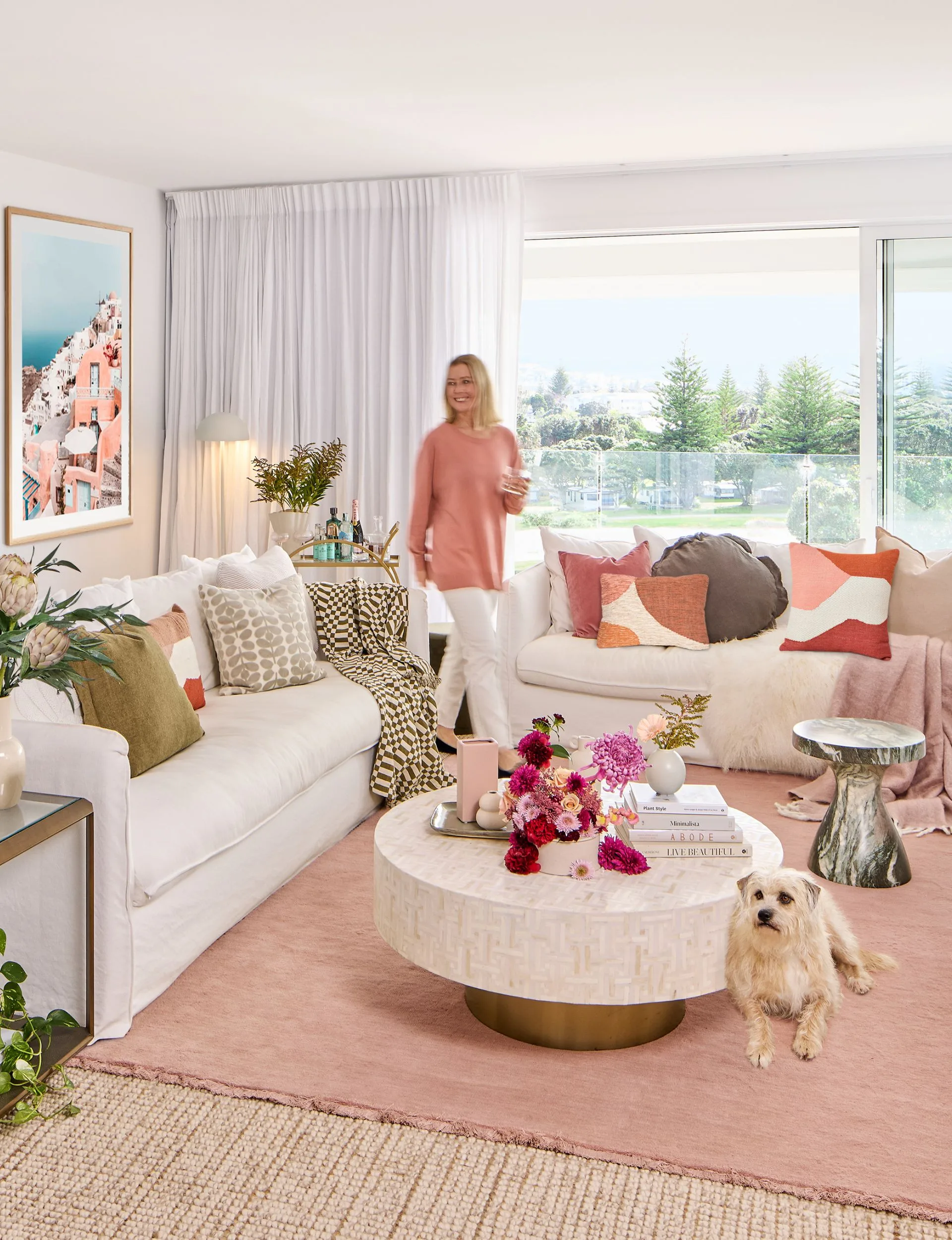 Woman walking through a cosy pastel pink themed living room covered in soft furnishings