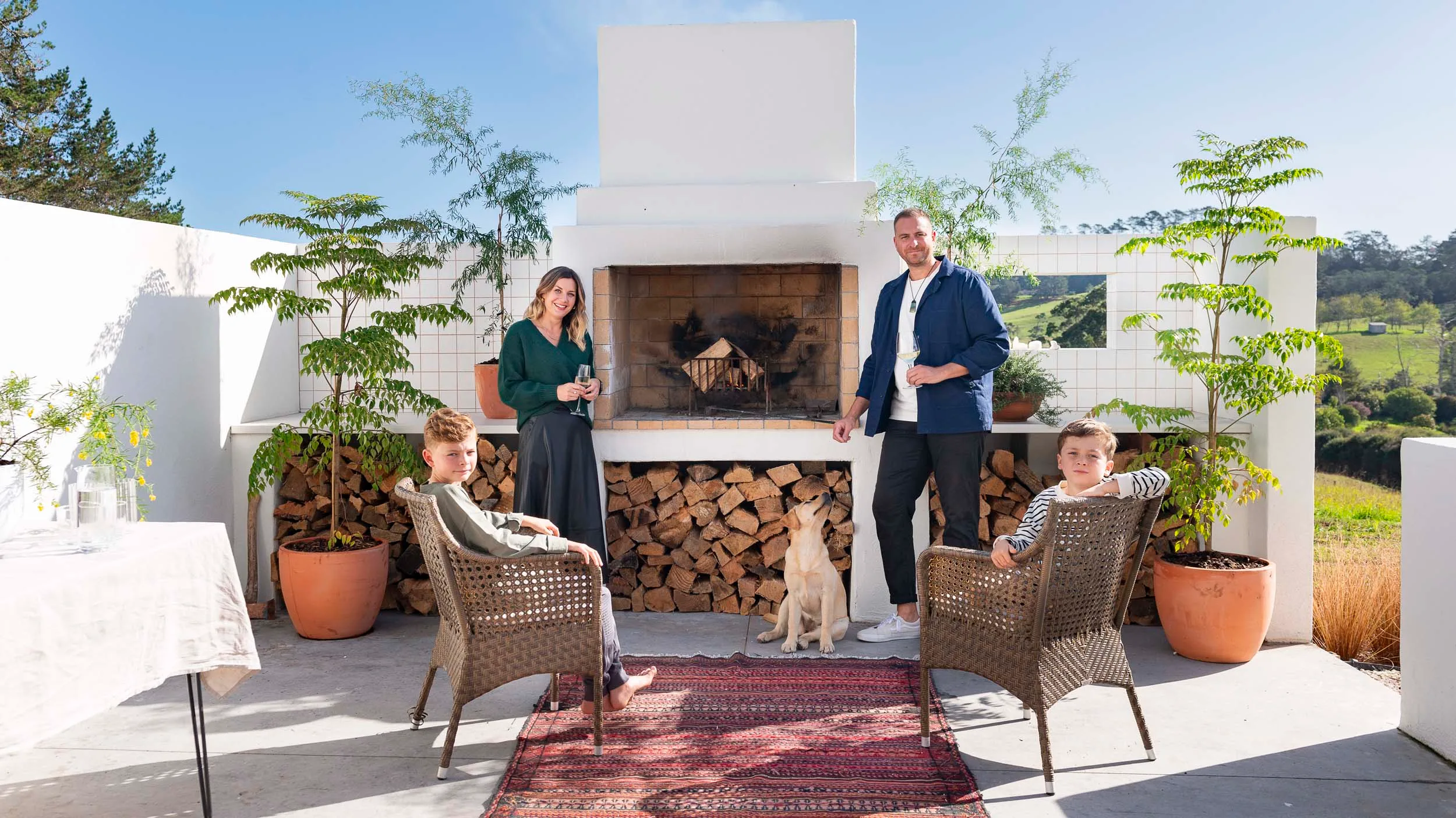 Rural home owners and their kids sitting around the outdoor fireplace of modern new build kumeu home