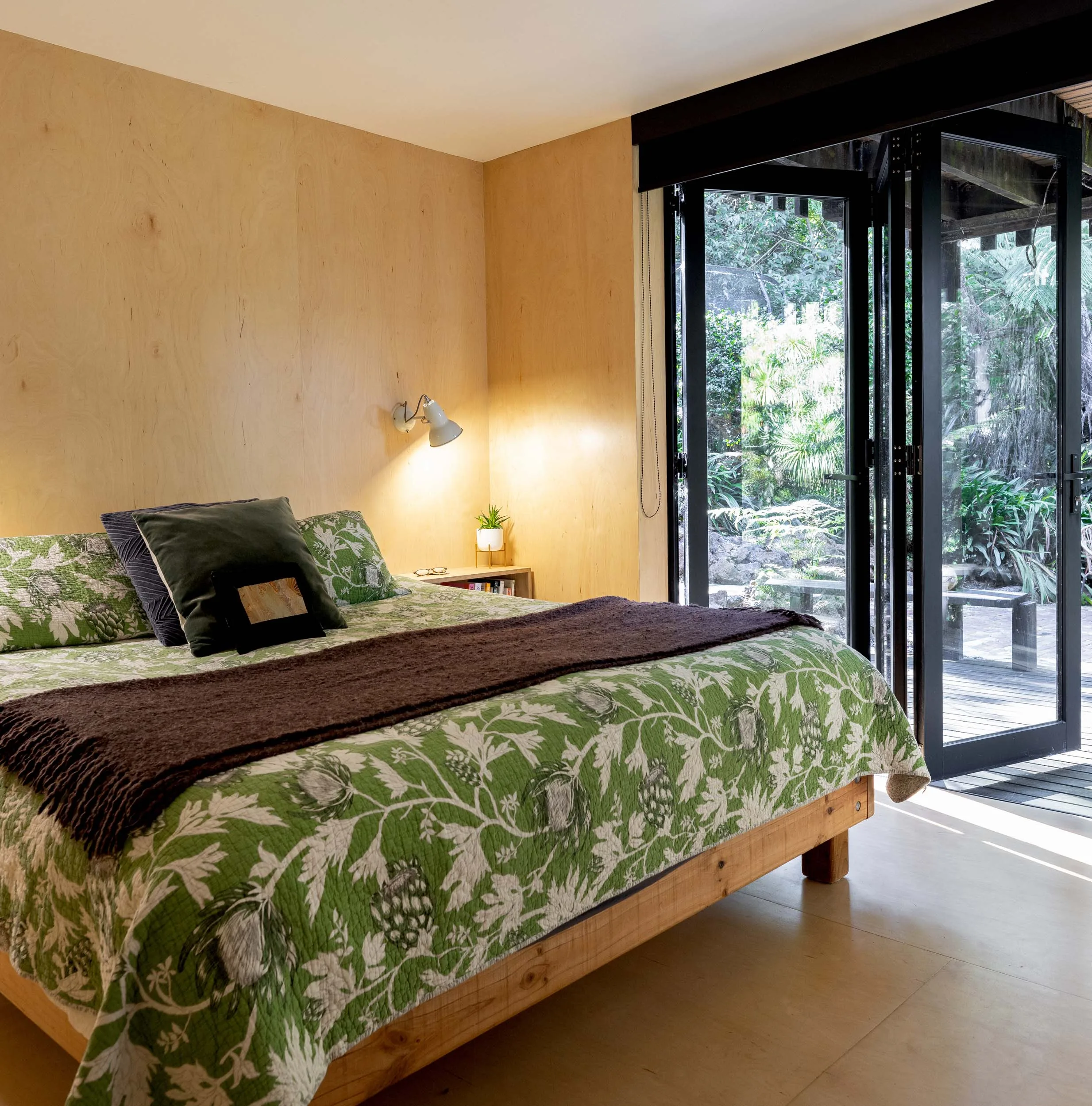 A relatively empty bedroom with a wide double bed against the middle of the back wall - green bedding over top