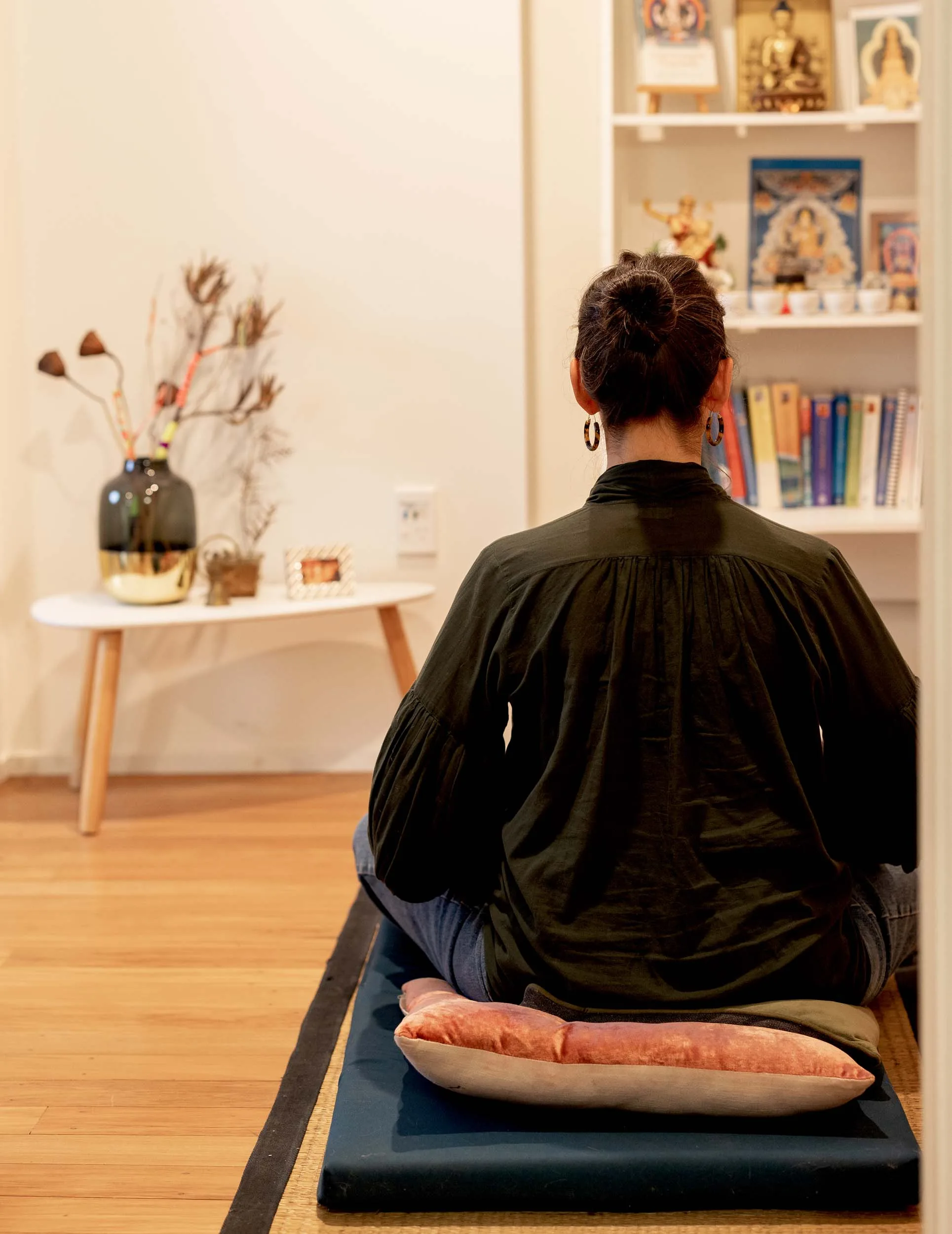 Titirangi home owner meditating with her back to the camera in front of a book shelf and side table