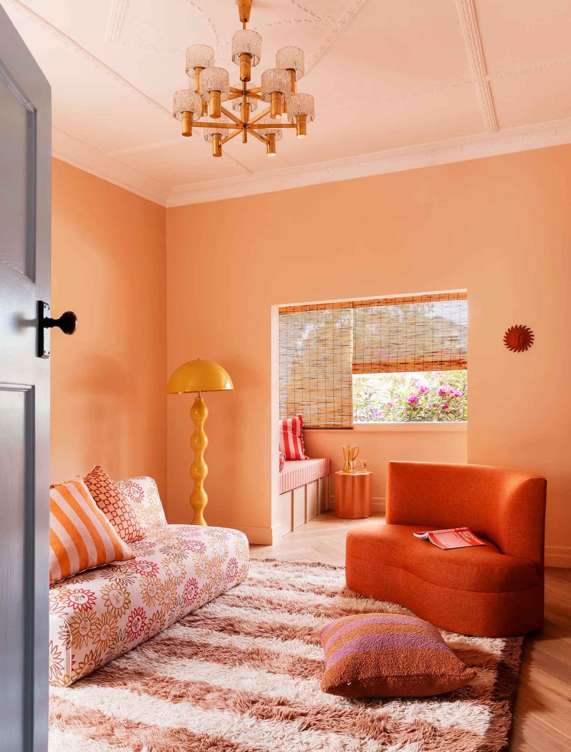 A salmon and orange living room viewed from the doorway, with a window seat through a second door frame on the other side of the room