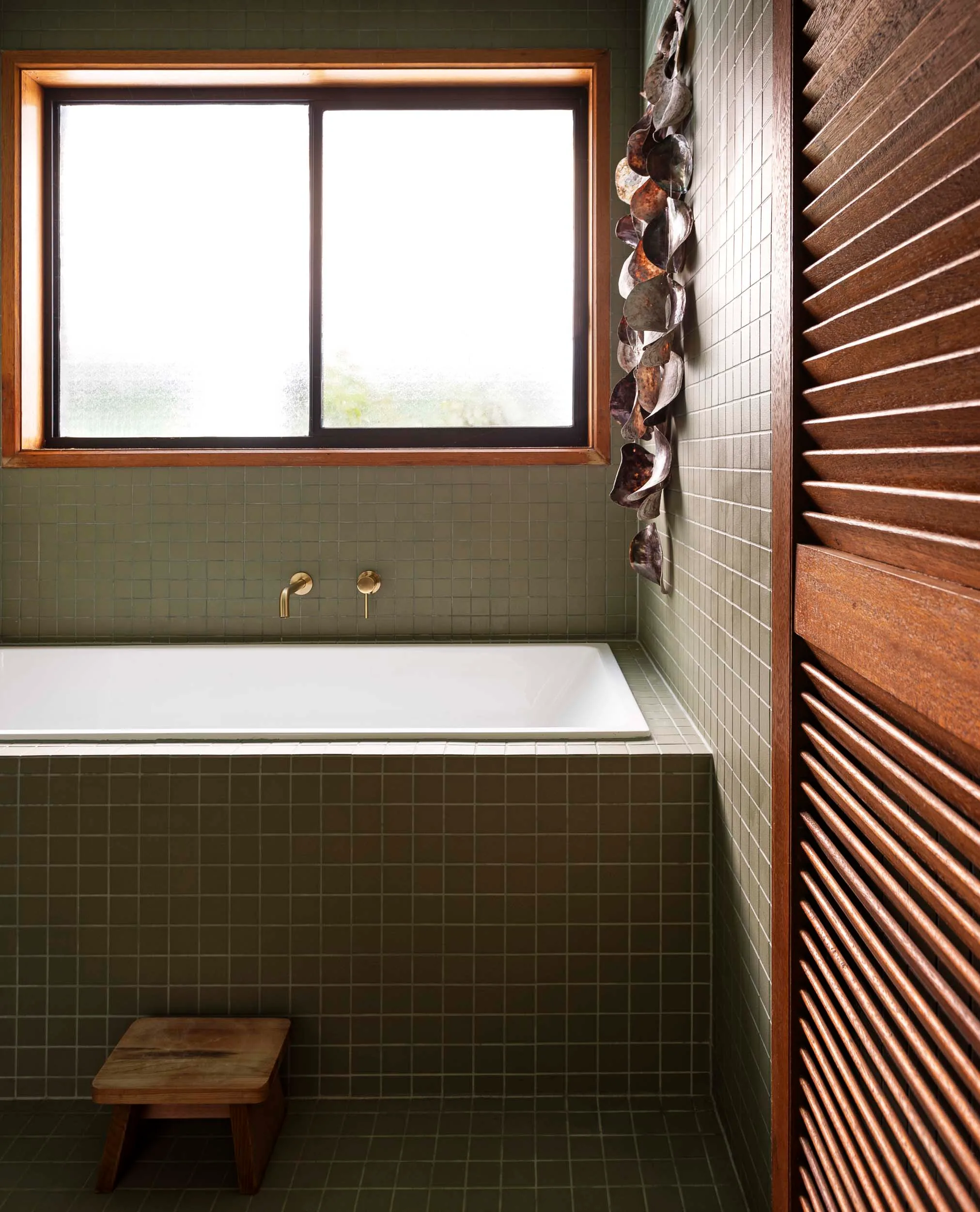 An olive green bathroom with a wooden slated door and a wooden windowsill