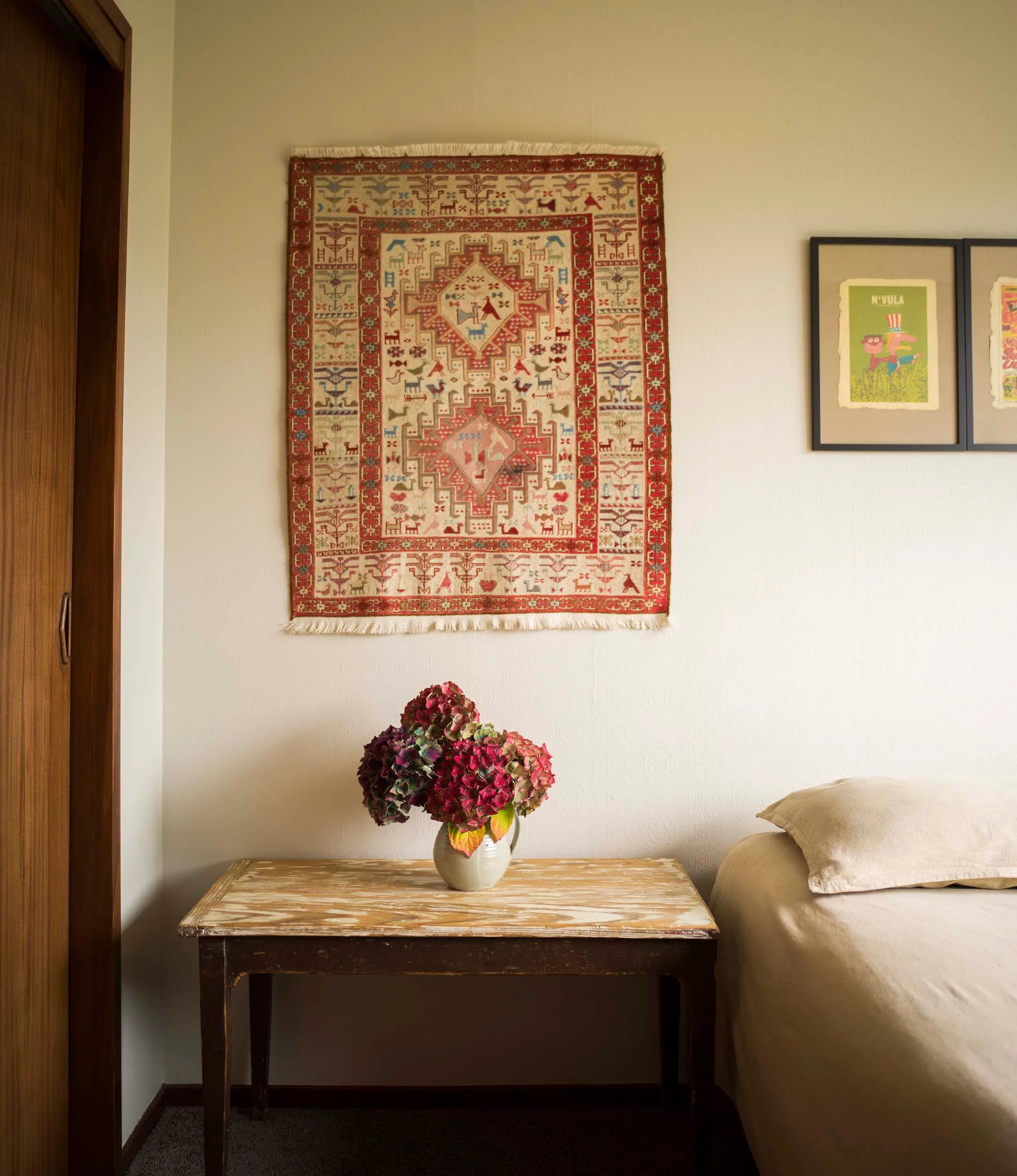A cream/white bedroom with an orange wall hanging over the bedside table