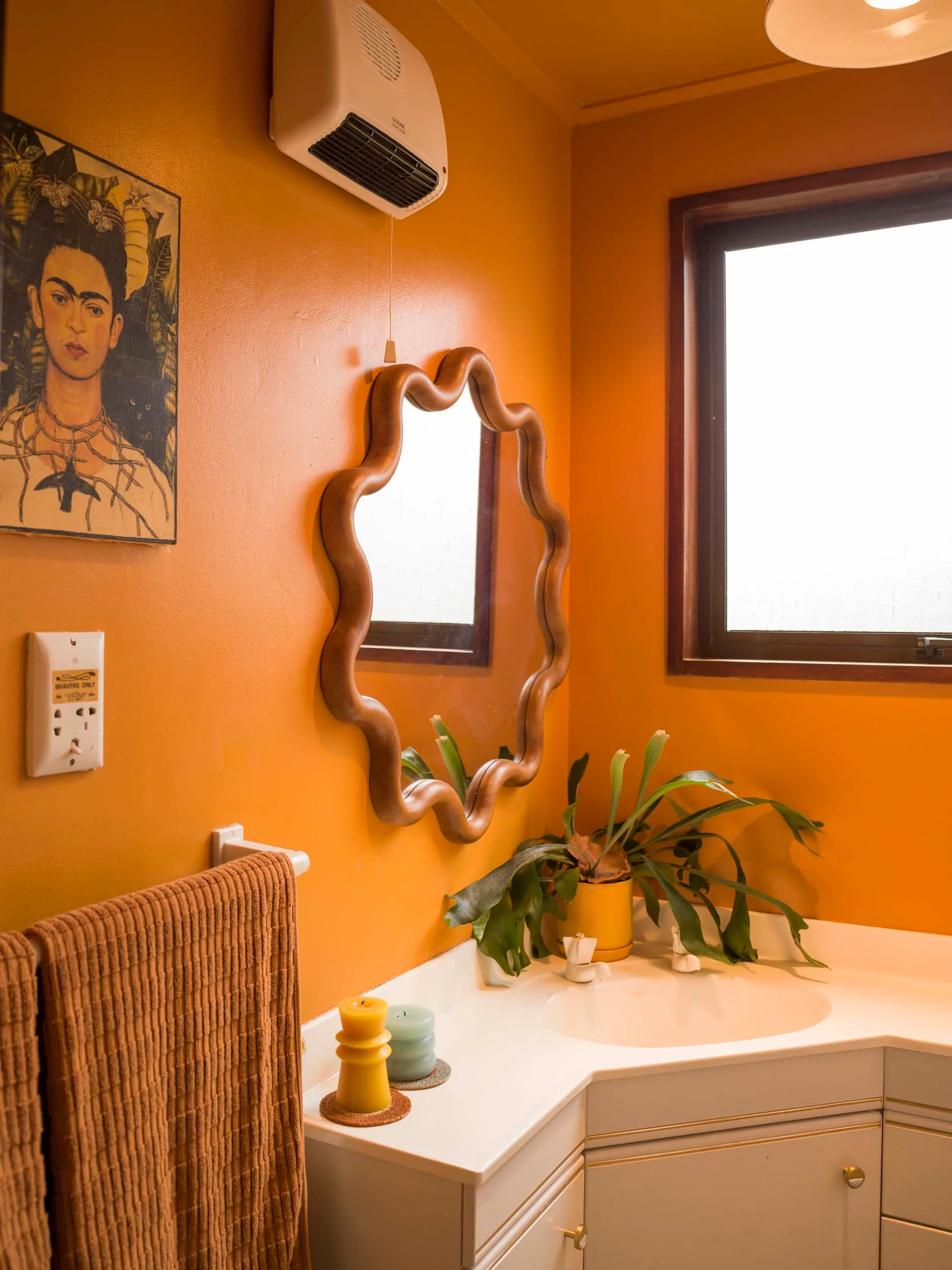 An orange bathroom with a squiggly round mirror above the vanity