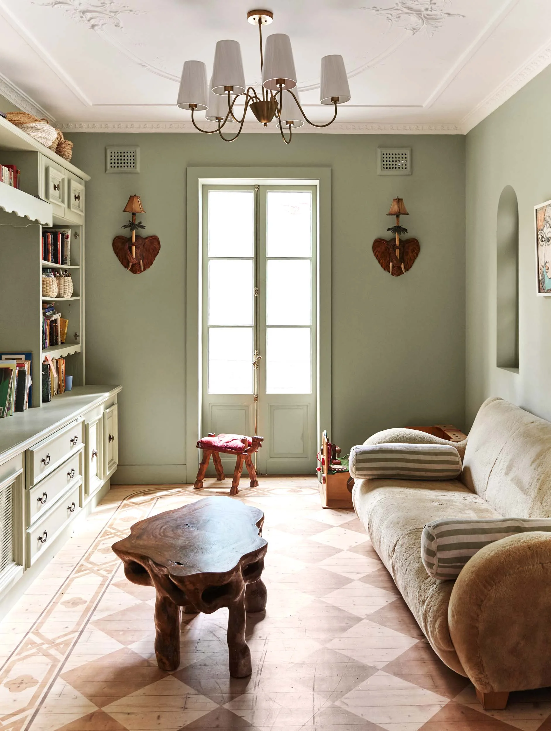 A rumpus room wirh dusty green walls and storage units, and pastel pink and white chequered tiles