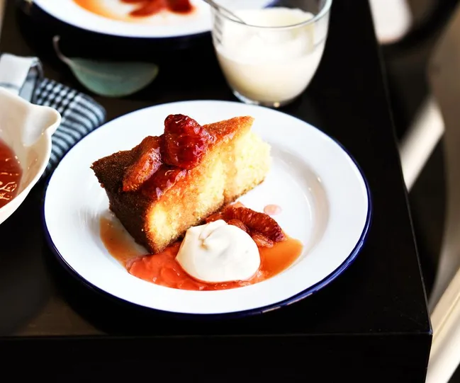 Slice of cake topped with blood orange slices and a dollop of cream on a white plate.