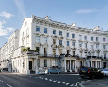 Street view of elegant white terraced Victorian townhouses with parked cars and a blue sky.