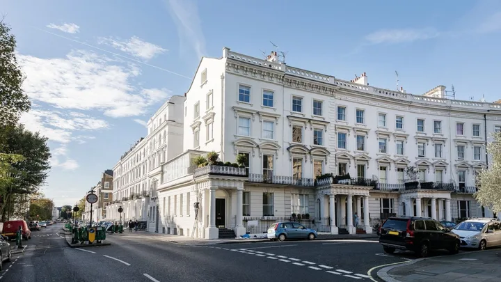 Street view of elegant white terraced Victorian townhouses with parked cars and a blue sky.