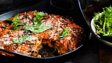 Eggplant parmigiana with basil and parmesan on top, served in a black serving dish