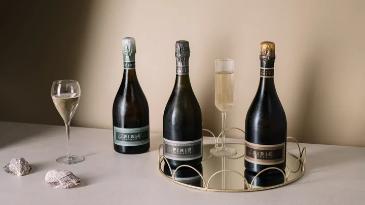 Three Pirie Tasmania sparkling wine bottles on a mirrored tray with two filled glasses and shells.