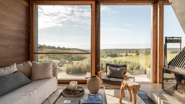 Airbnb Victoria interior featuring open-plan living room with fireplace and adjacent dining room, with views out to rolling hills