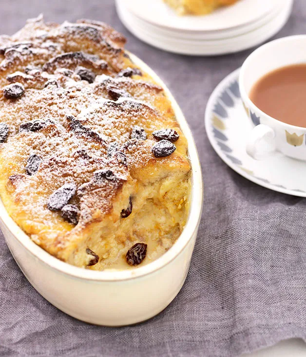Bread and butter pudding in a white oval dish on a grey linen tablecloth.