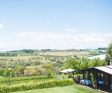 A panorama shot showing a light blue sky with clouds and rolling green hills, and in the foreground, in the bottom right, the covered outdoor seating section of a restaurant.
