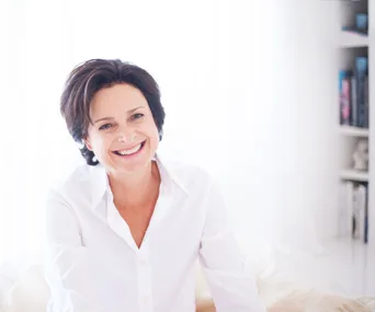 Publisher Julie Gibbs smiling in a white button shirt, with a white background and a bookshelf in the background.