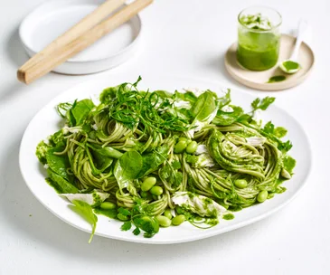 A white plate with soba noodles, chicken, edamame, spring onion and coriander. 