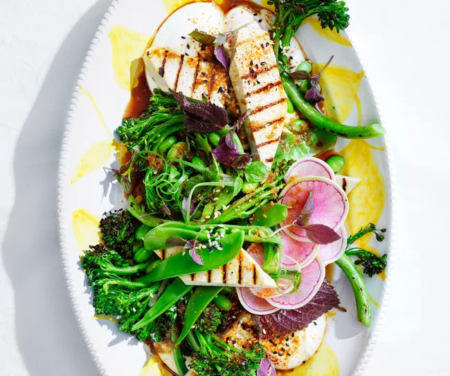 Grilled halloumi salad with radishes, sugar snap peas, broccolini, and sesame seeds on a decorative white platter.