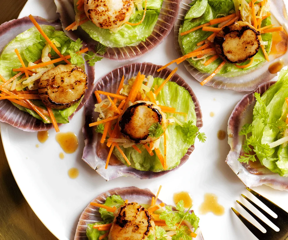 Six scallops served in half of their shells on a bed of lettuce, carrot, and water chestnuts.