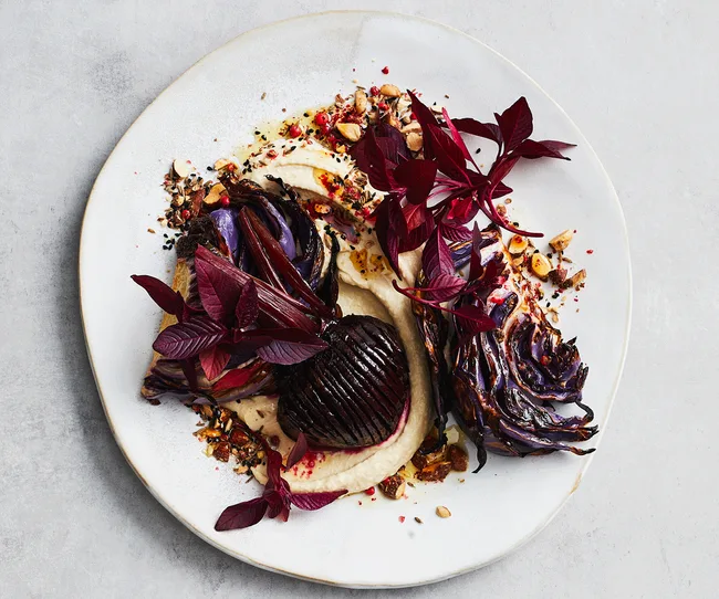 Roasted beetroot with purée and herbs, garnished with red leaves and nuts, served on a white plate.