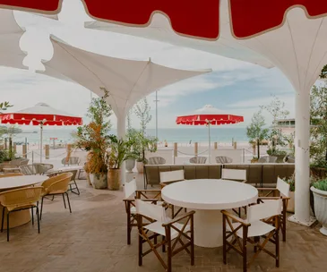 Promenade Bondi Beach's outdoor terrace with beach views, white tables, tiled flooring and white and red sun umbrellas