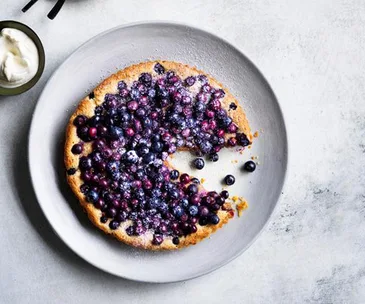 Blueberry tart, with a slice taken out of it, on a grey plate