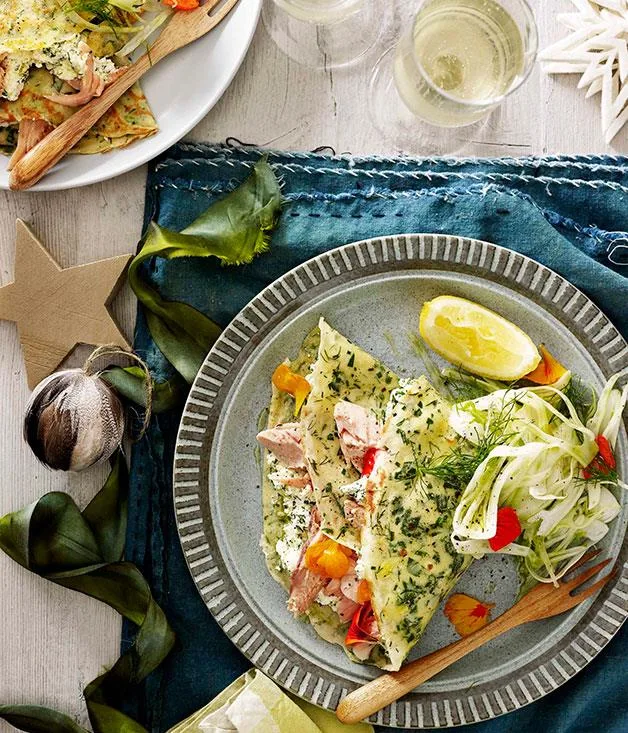 Plate of smoked trout crepes with dill, salad, and a lemon wedge, on a blue napkin with wooden cutlery.