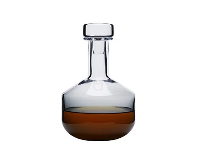 Glass decanter with a stopper, half-filled with brown liquid, on a white background.