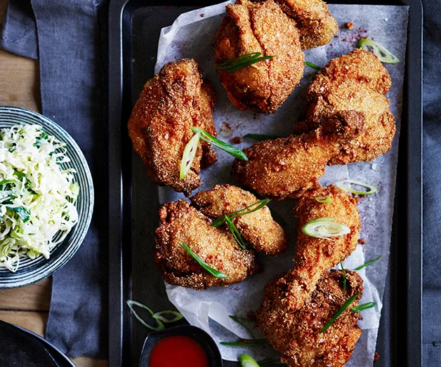 Crispy fried chicken with sliced green onions on a tray, served with coleslaw and a side of hot sauce.