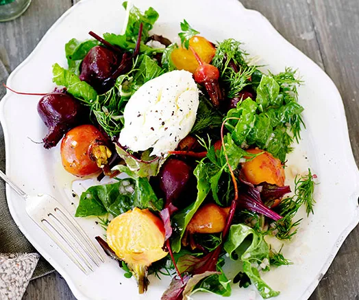 Fresh salad with roasted beets, mixed greens, a dollop of goat cheese on a plate, garnished with herbs, fork beside.