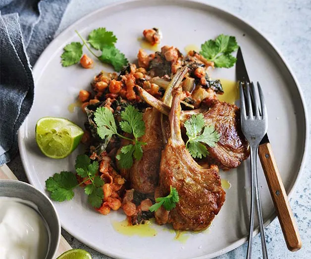 Grilled lamb chops with chickpeas, greens, cilantro, lime, and a side of yogurt on a white plate.