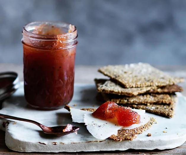 Jam jar, spoon, and crackers with cheese on a tray.