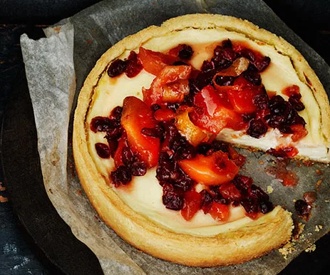 Cheesecake topped with fresh sliced plums and cherries on parchment paper, with a slice missing.