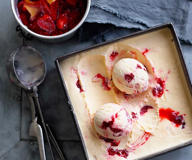 Two scoops of vanilla and raspberry ripple ice cream in a tray, with a bowl of berry sauce and a scoop on the side.