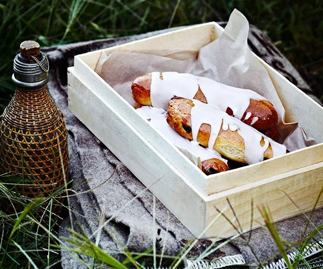 A wooden box with glazed pastries and a wicker bottle on grass.