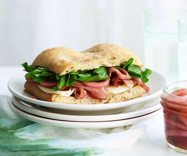 Sandwich with sliced meat, cheese, and greens on ciabatta bread, served on a white plate.