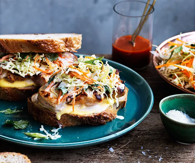 Grilled chicken sandwiches with coleslaw on a blue plate, served with sauce and salt on a wooden table.