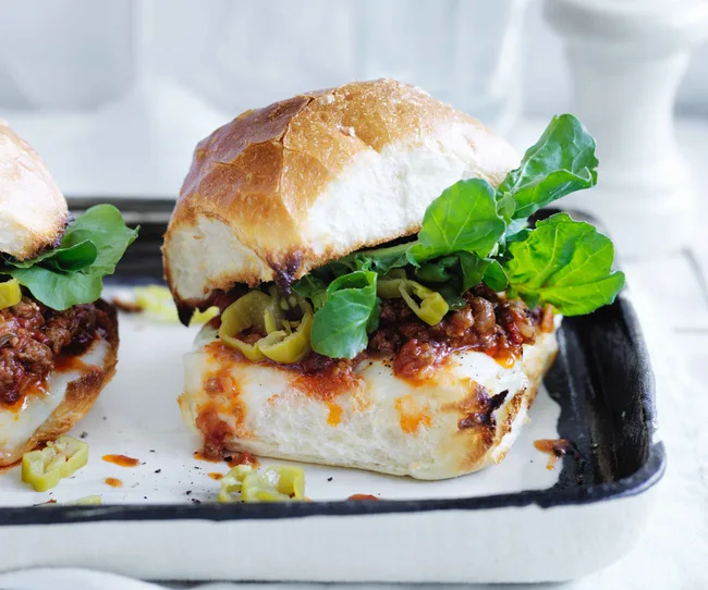 A sandwich with melted cheese, spicy beef, arugula, and peppers on a toasted bun.