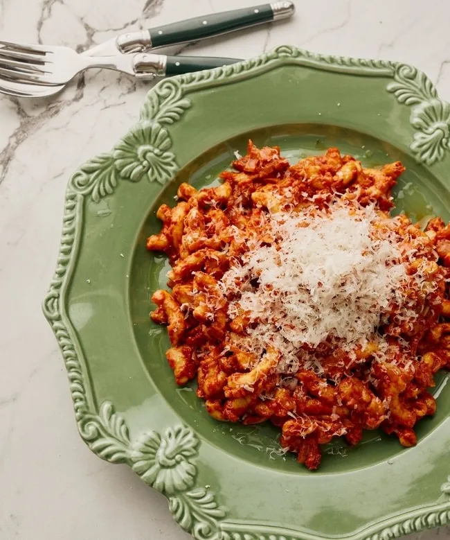 Pasta with tomato sauce and grated cheese on a green decorative plate, placed on a marble surface.