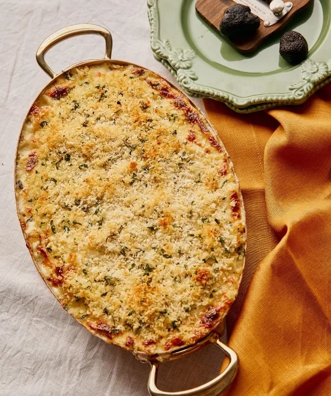 Baked truffle mac and cheese in an oval dish with golden crust, next to a plate with truffles and cheese on the side.