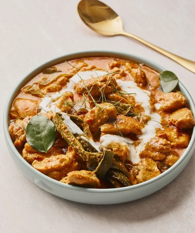 Creamy Thai red curry with chicken, garnished with herbs and served in a bowl, with a gold spoon beside it.