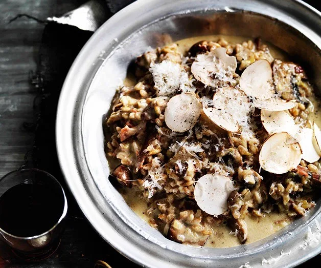 A bowl of creamy risotto with mushrooms and shaved truffle, garnished with grated cheese.