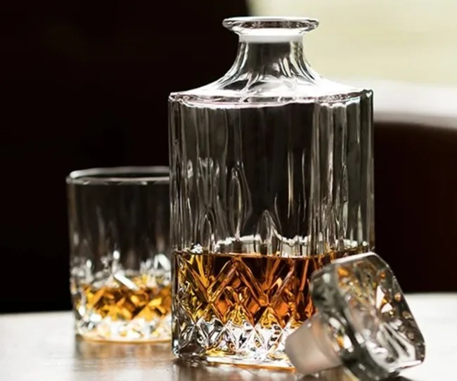 Decanter and glass on table, filled with amber liquid, natural light.