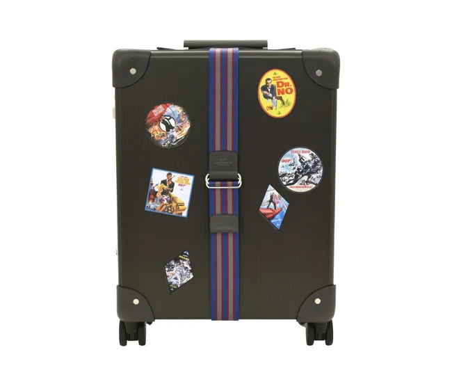 Black suitcase with colorful James Bond movie stickers and a red-blue stripe strap.