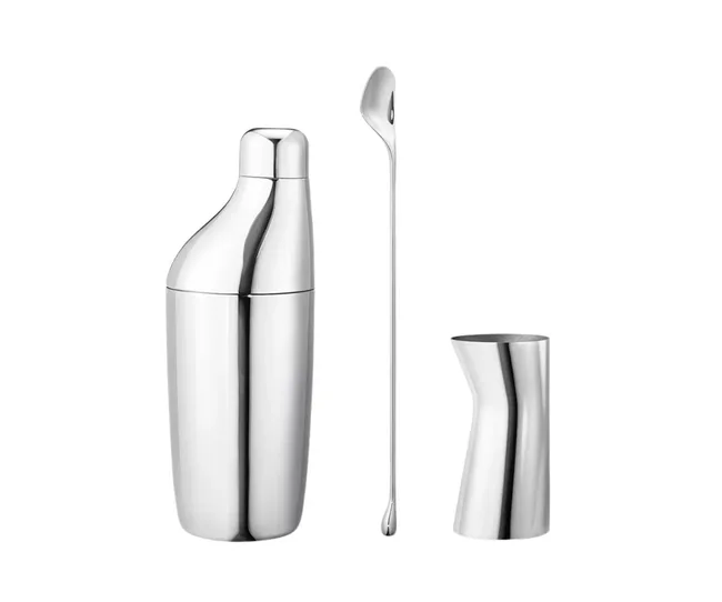 Stainless steel cocktail shaker, stirring spoon, and jigger set on a white background.